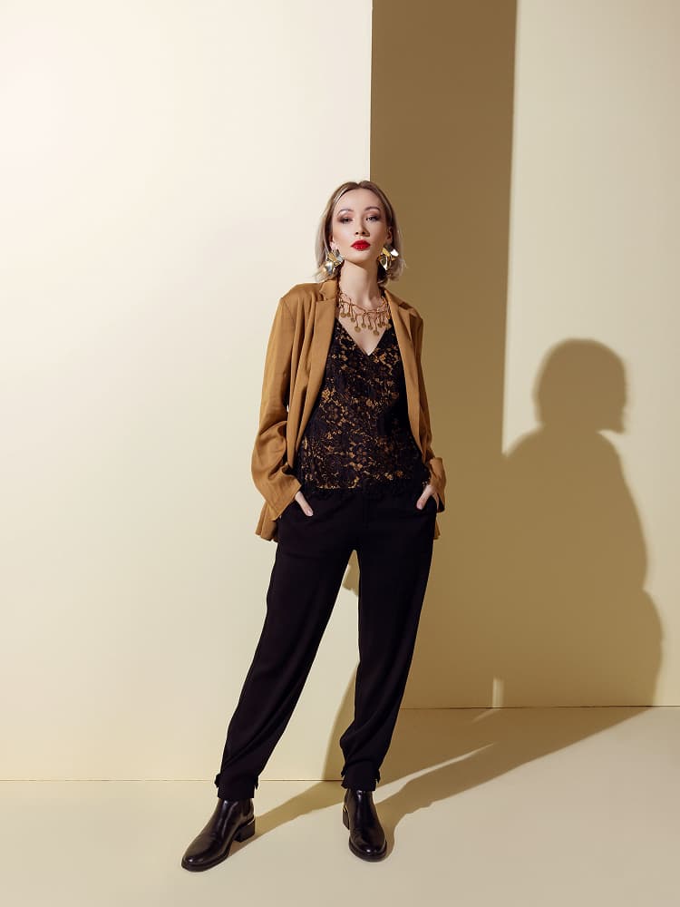 A model wearing a delicate black floral lace camisole under a structured camel-colored tailored blazer with black trousers.