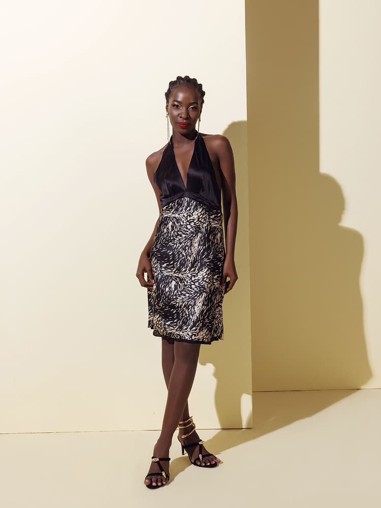 A model wearing a black silk halter neck bodice joined with a stylized animal print silk skirt, featuring a deep V-neckline.