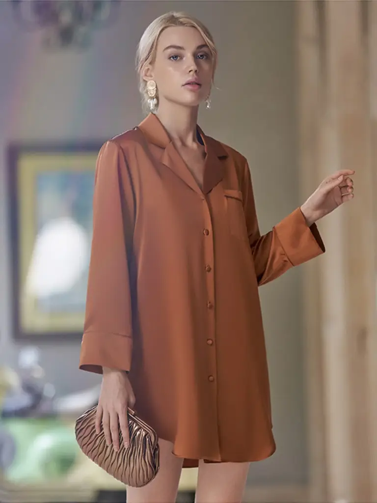 A model wearing a bronze-colored silk button-down lounge dress, highlighting the fluid drape and rich metallic sheen.
