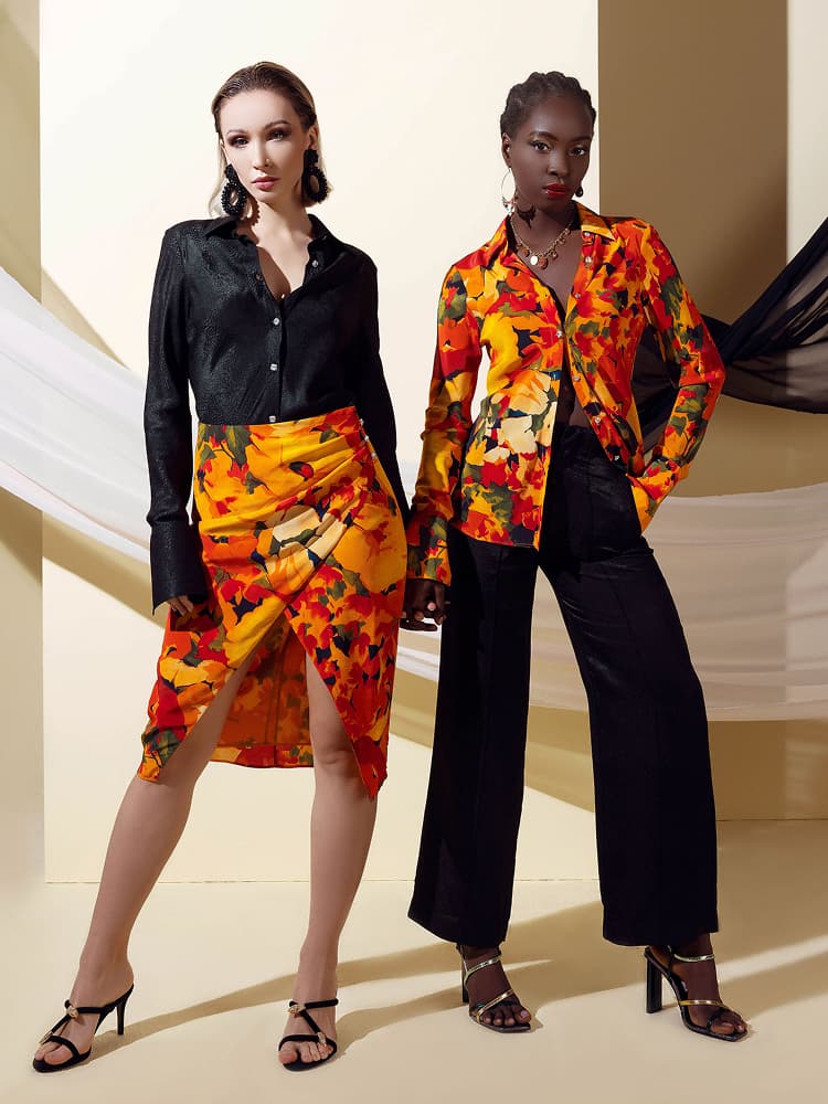 Two models showcasing the Summer Flower silk collection, featuring a tailored floral shirt, a matching wrap-style skirt, and coordinated black trousers.