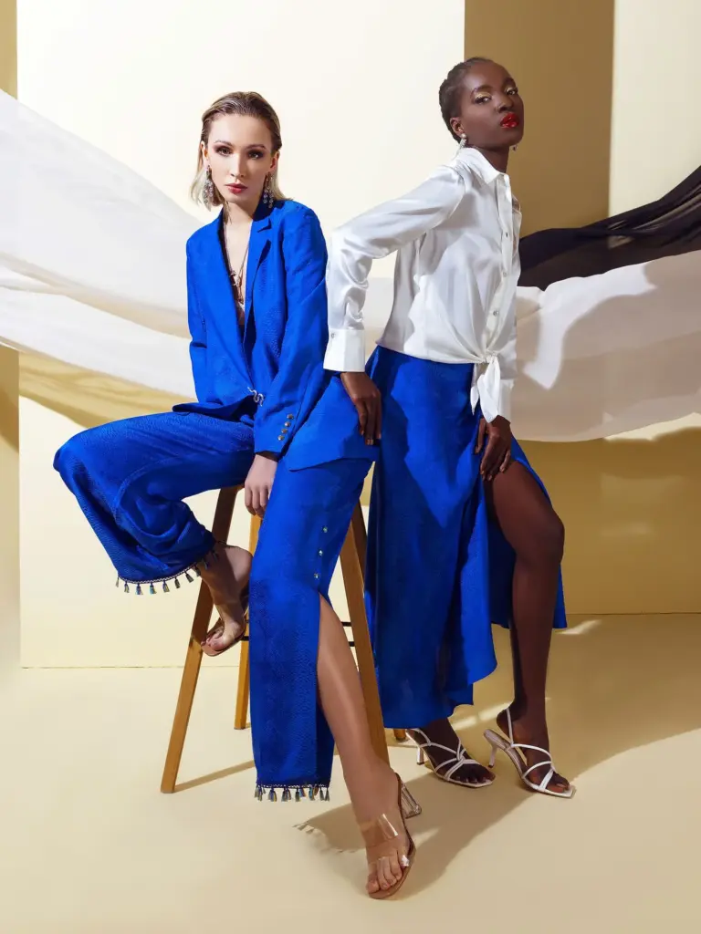 Two models showcasing the Deep Blue Viscose Jacquard collection, featuring a tailored blazer, trousers with tassel details, and a high-slit skirt.