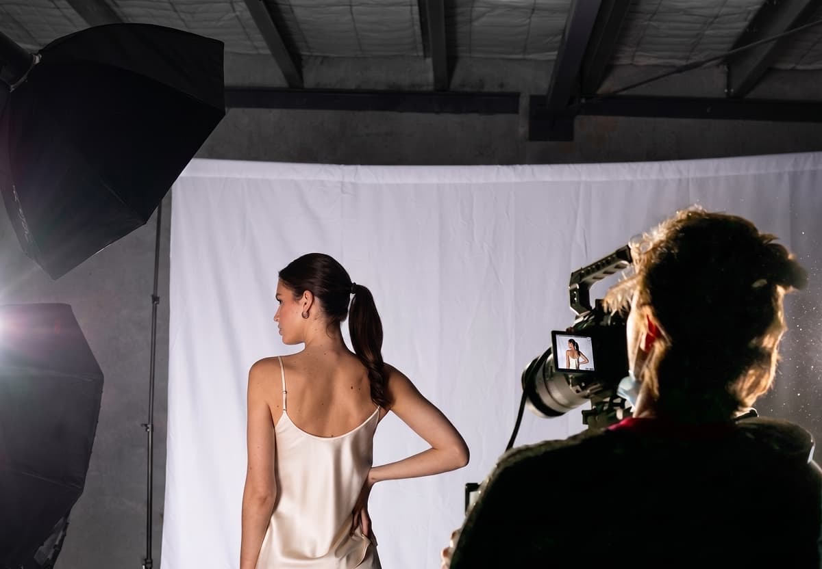 Photographer shooting a model wearing a silk slip dress in a professional fashion photography studio with white backdrop